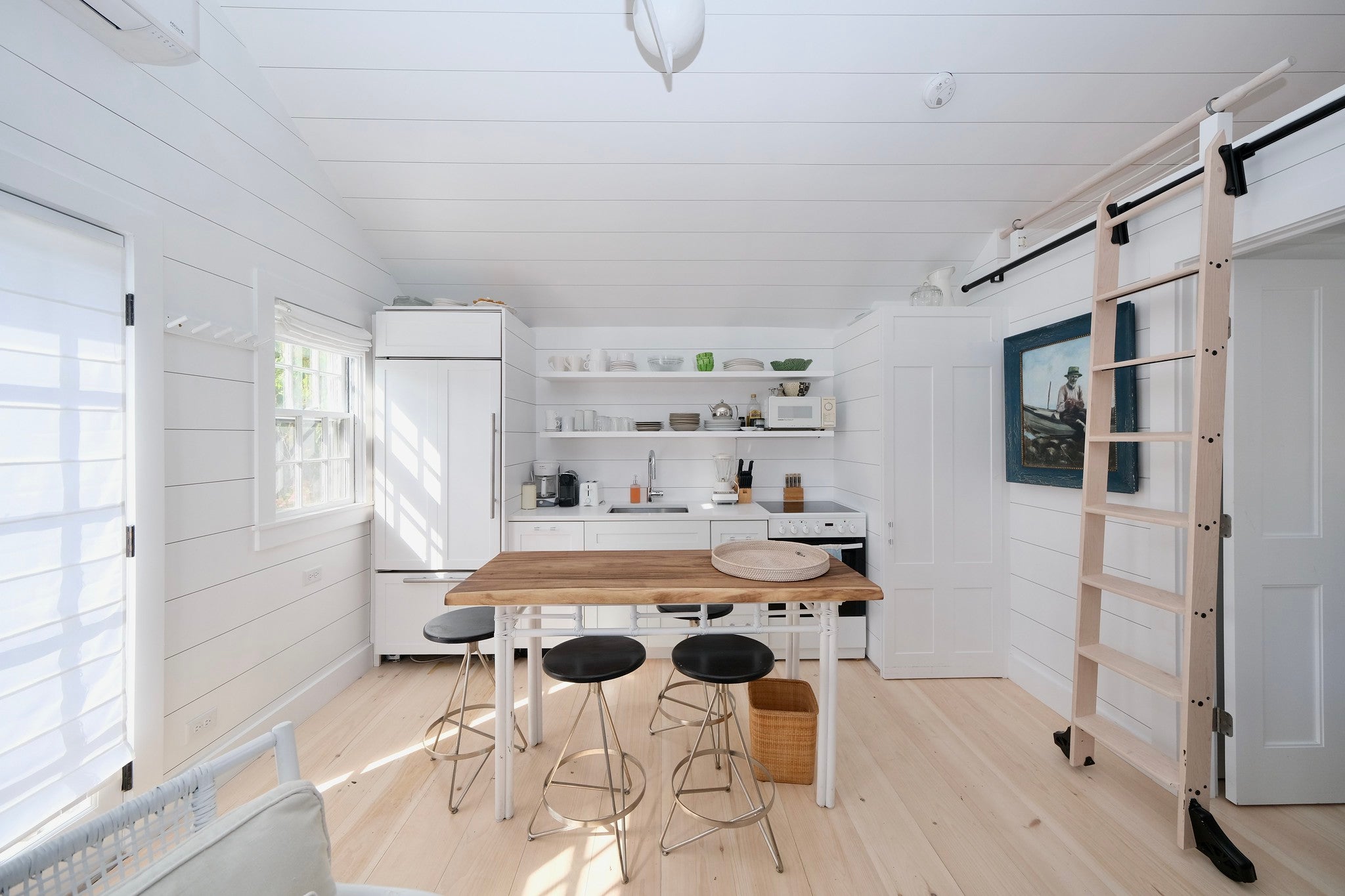 White shiplap walls, a long table with stools, white metal furniture, and white appliances.