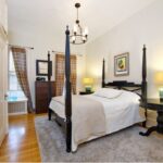 A bedroom with white walls, two windows, wood flooring, and a four-poster bed.