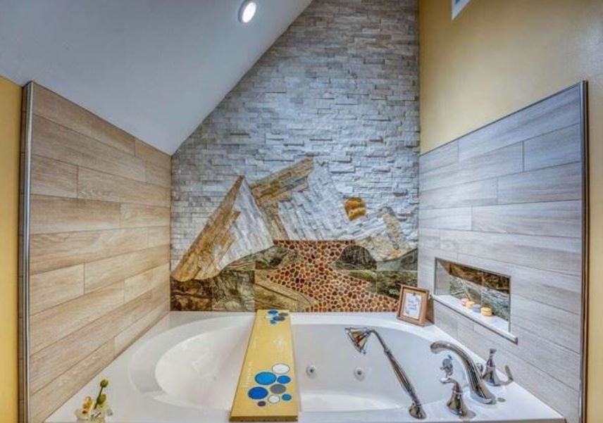 A soaking tub with an angled wall of mosaic tile depicting a mountain scene.