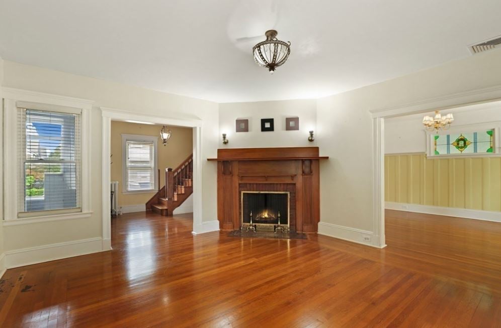 View of room with white walls, hardwood flooring, and a redbrick fireplace.