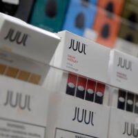 alt = white boxes of Juul products are displayed at a smoke shop in New York in 2018