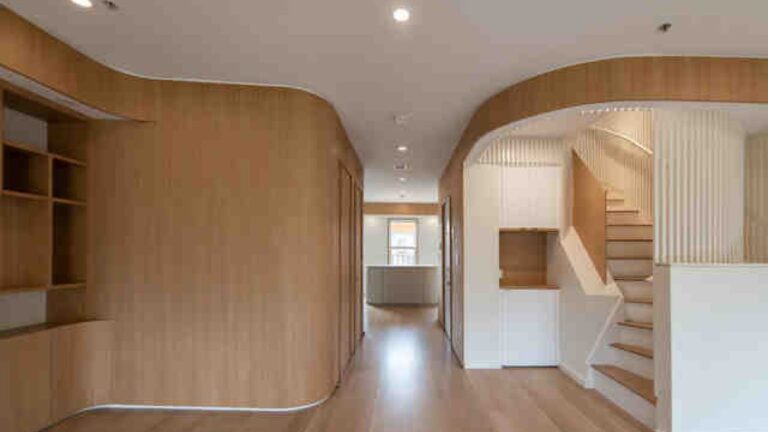 A view of curvy wood-clad and white walls into the kitchen. The room is unfurnished.