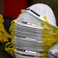 alt = stack of white N-95 masks with yellow elastics