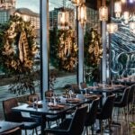 At Nautilus Pier 4 in the Boston Seaport, tables along floor-to-ceiling windows decorated for Christmas with green and gold wreaths.