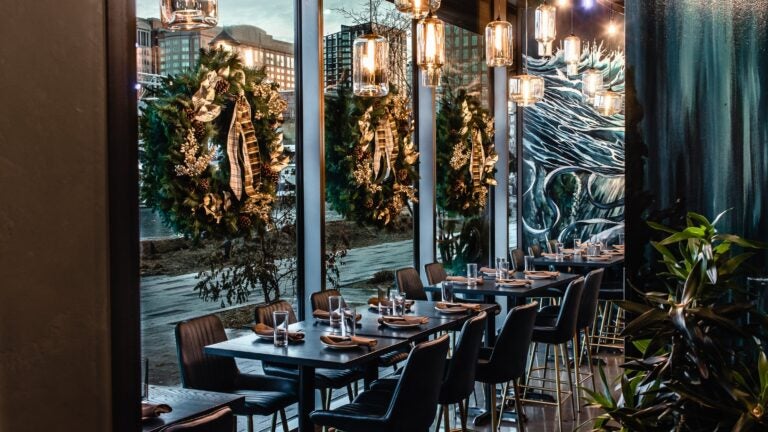 At Nautilus Pier 4 in the Boston Seaport, tables along floor-to-ceiling windows decorated for Christmas with green and gold wreaths.