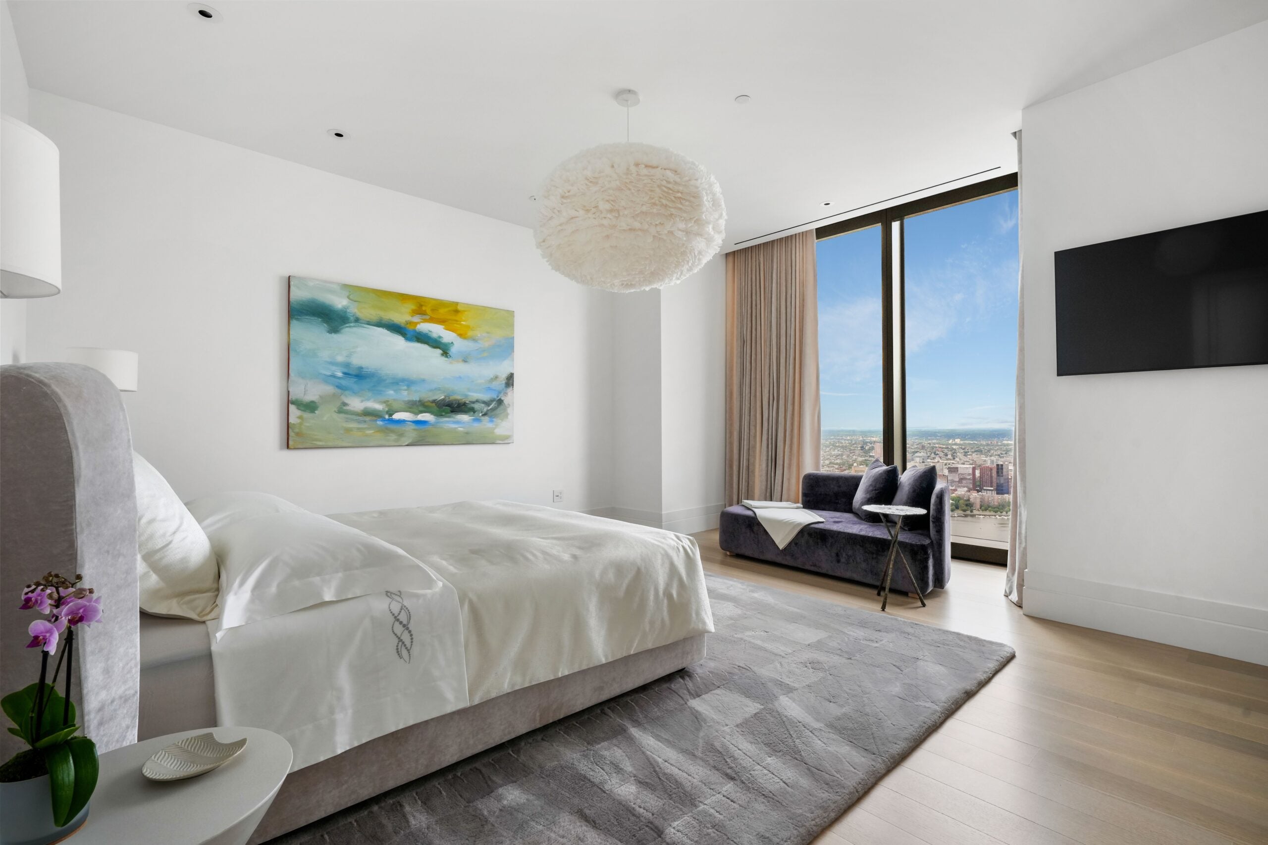 One Dalton primary bedroom with bed, chandelier and large window wall.