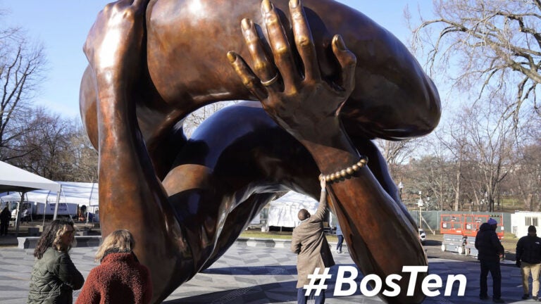 A man reaches to touch a detail of the 20-foot-high bronze sculpture "The Embrace," a memorial to Dr. Martin Luther King Jr. and Coretta Scott King, in the Boston Common, Tuesday, Jan. 10, 2023, in Boston. The sculpture, consisting of four intertwined arms, was inspired by a photo of the Kings embracing when MLK learned he had won the Nobel Peace Prize in 1964. The statue is to be unveiled during ceremonies Friday, Jan. 13, 2023.