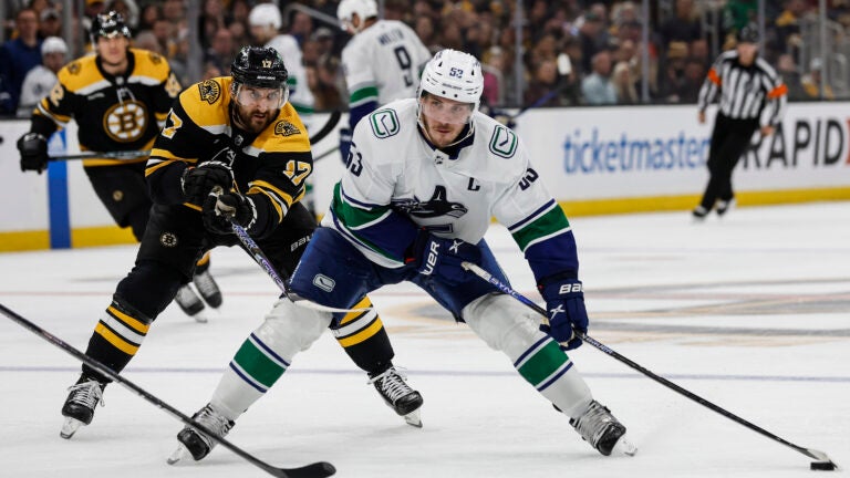 Boston Bruins' Nick Foligno (17) tries to slow down Vancouver Canucks' Bo Horvat during the third period of an NHL hockey game Sunday, Nov. 13, 2022, in Boston.