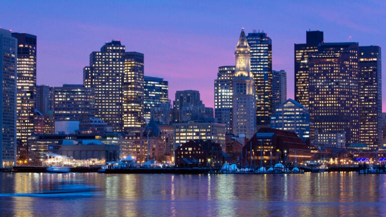 The Boston skyline is illuminated and reflected in the waters of Boston Harbor.