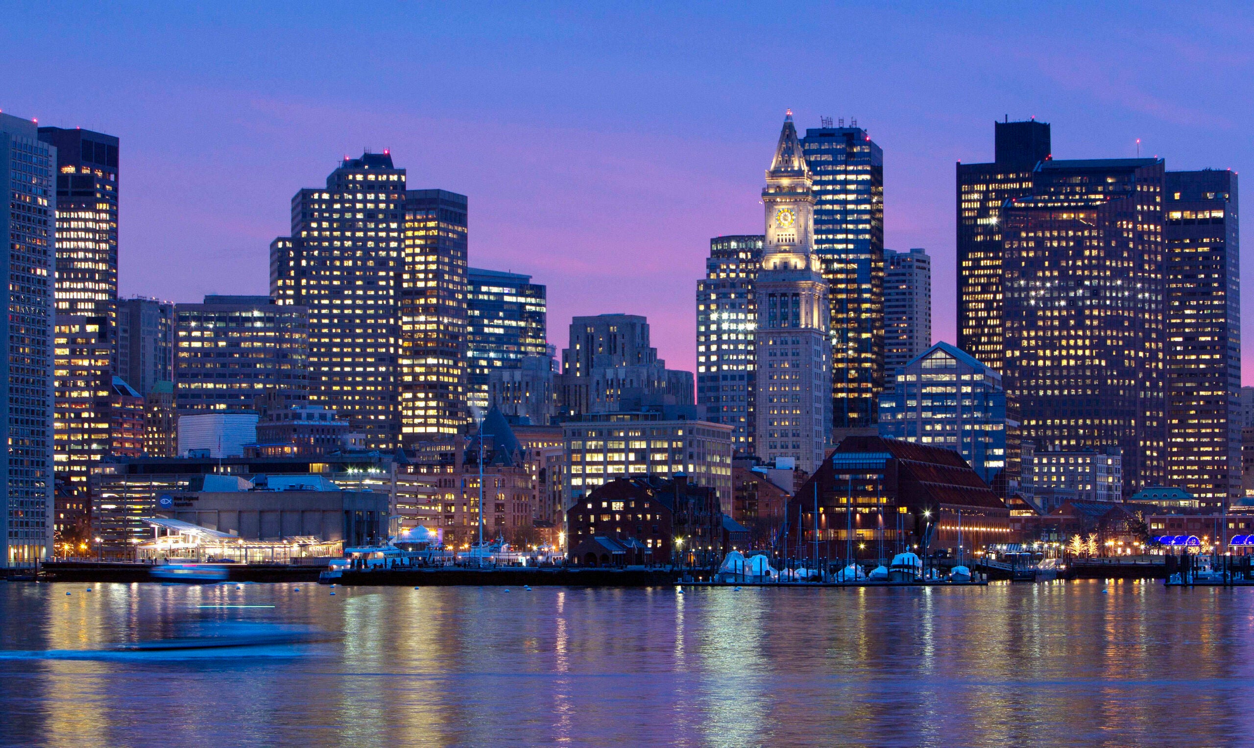 The Boston skyline is illuminated and reflected in the waters of Boston Harbor.