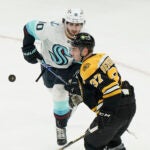 Seattle Kraken center Matty Beniers (10) and Boston Bruins center Patrice Bergeron (37) keep their eyes on the puck in the second period of an NHL hockey game, Thursday, Jan. 12, 2023, in Boston.