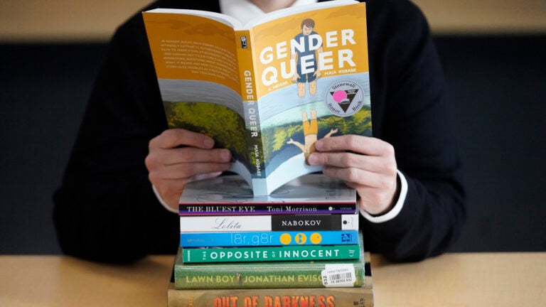 alt = Amanda Darrow, director of youth, family and education programs at the Utah Pride Center, poses with books that have been the subject of complaints from parents in Salt Lake City on Dec. 16, 2021.