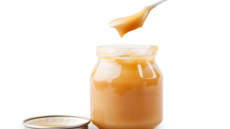 alt = a spoon lifts orange baby food out of a jar with a lid sits next to it