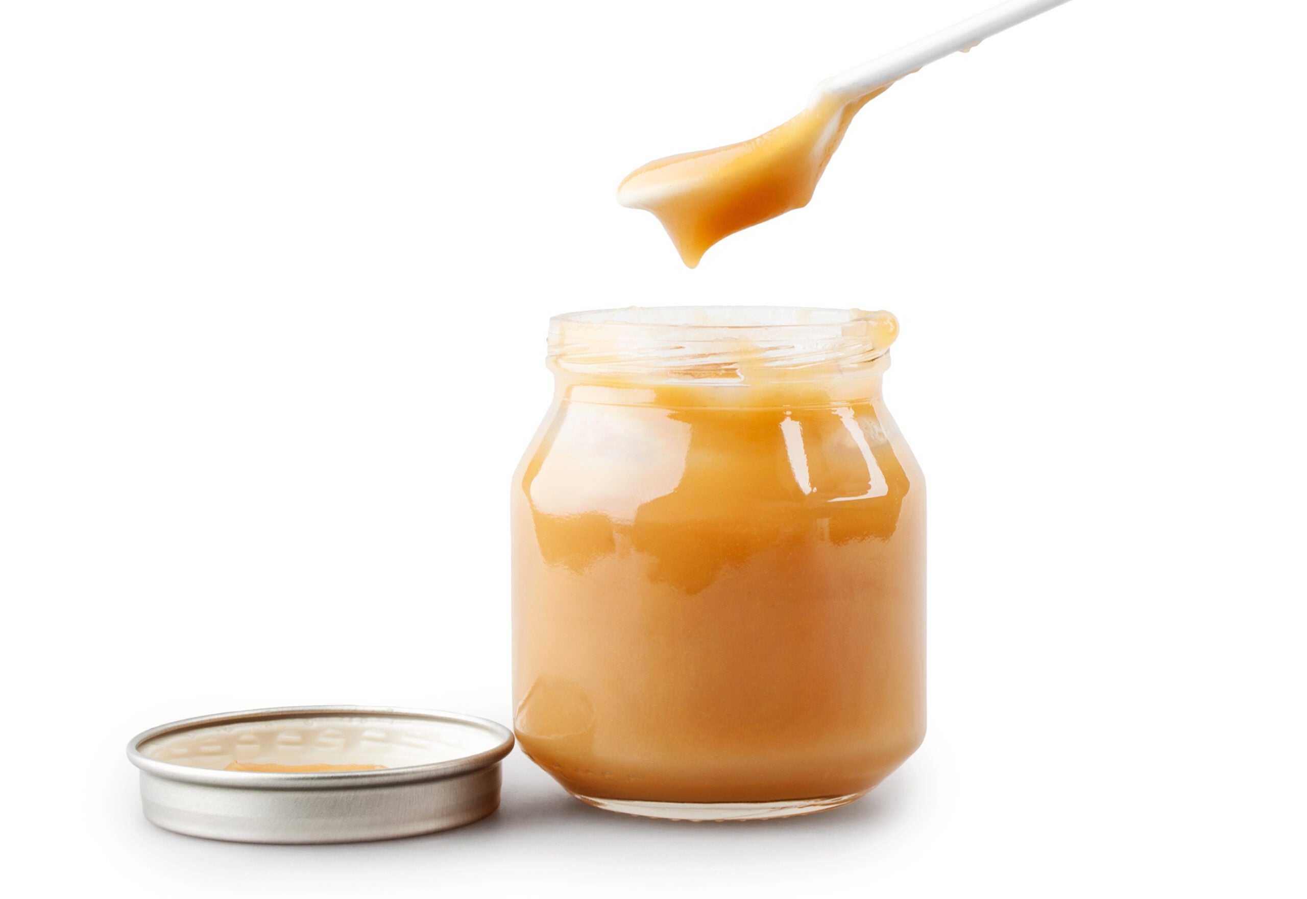 alt = a spoon lifts orange baby food out of a jar with a lid sits next to it