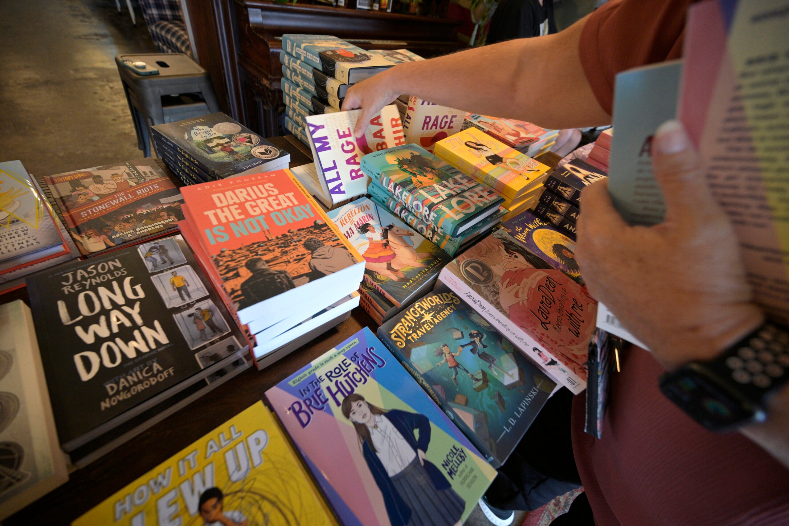 alt = a school librarian's hand reaches out to flip through titles from a table of books at a book giveaway in Florida last summer.