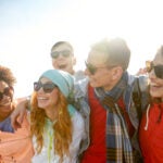 alt = group of smiling teens wearing sunglasses with their arms around one another