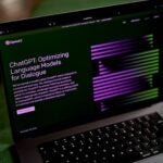 alt = The OpenAI website ChatGPT with a black background and purple and green font on a black laptop computer.