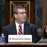Michael A. Delaney — shown seated at a table in a suit and tie, a name plate in front of him — at his Senate Judiciary Committee hearing on Feb. 15, 2023.