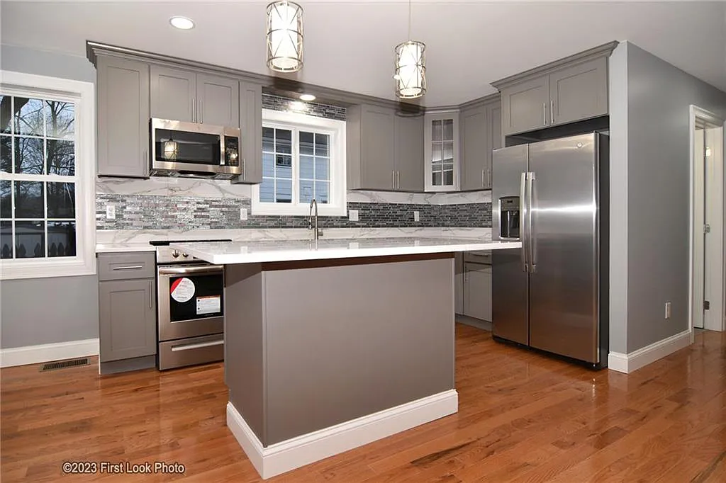 The kitchen has hardwood floors, gray tile backsplash, marble countertops, gray cabinets and stainless steel appliances.