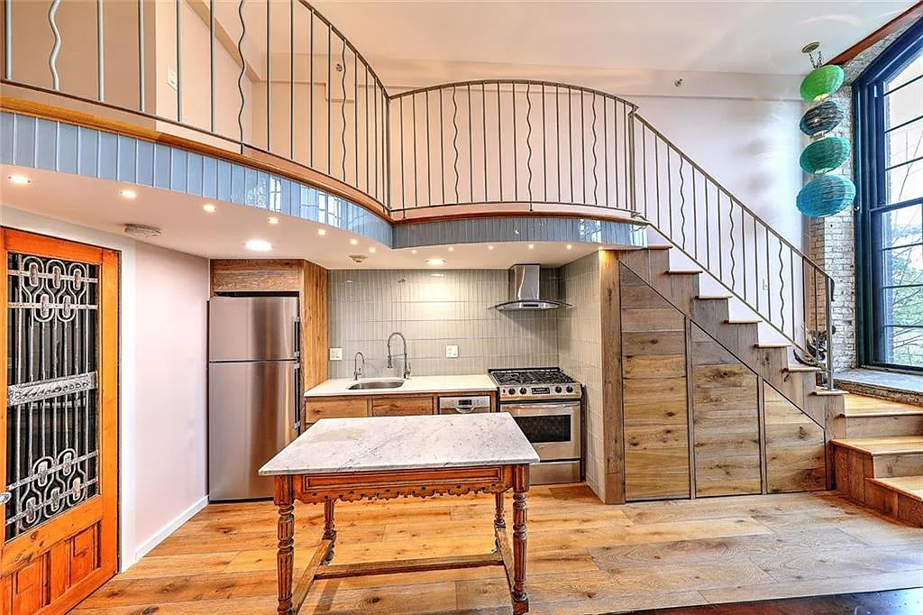 A staircase above the kitchen leads to a lofted bedroom and bathroom.