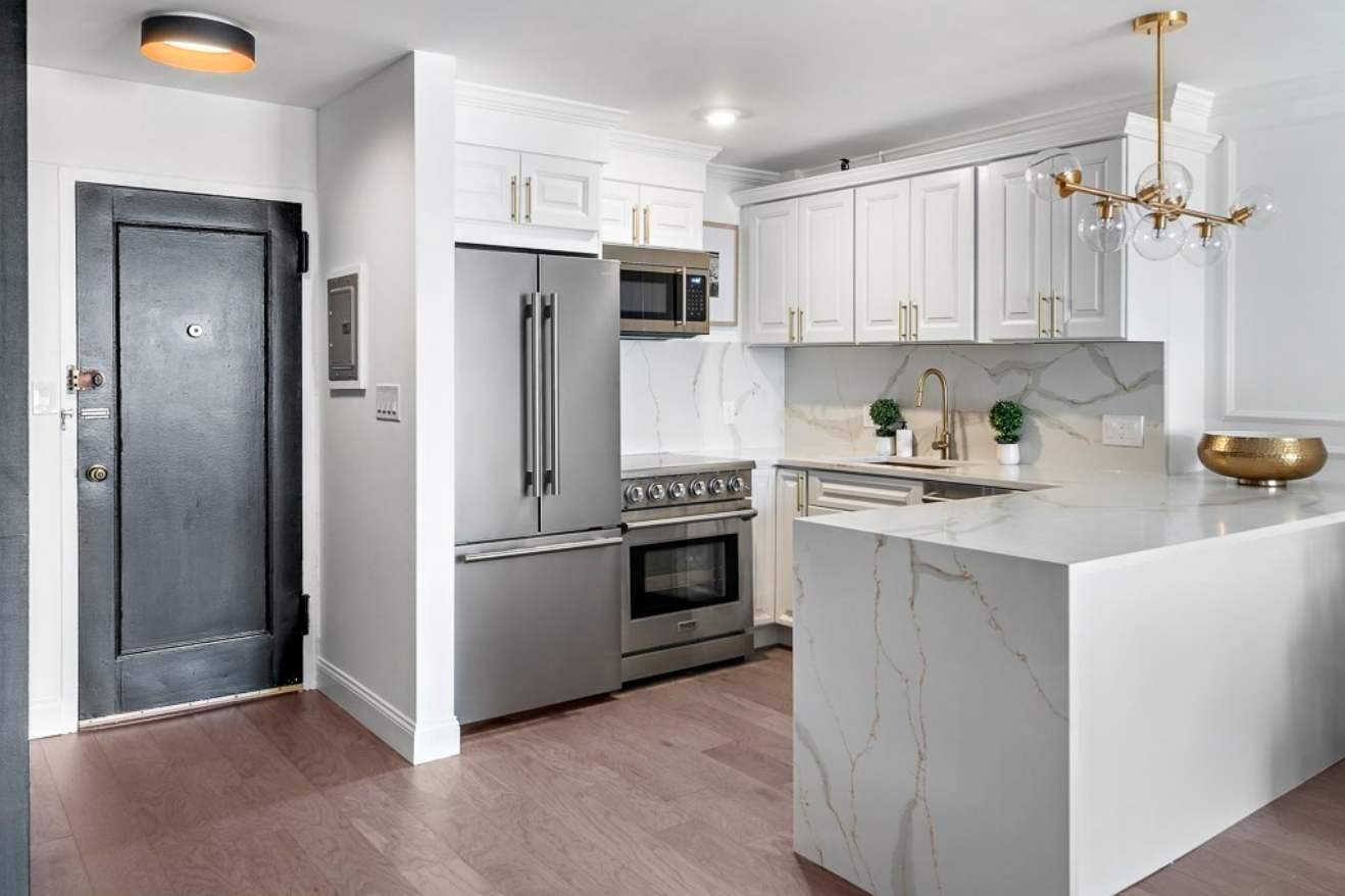 The kitchen has white cabinets with gold hardware, stainless steel appliances, and hardwood floors.