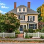 A peach-colored Victorian with green shutters and a white picket fence.