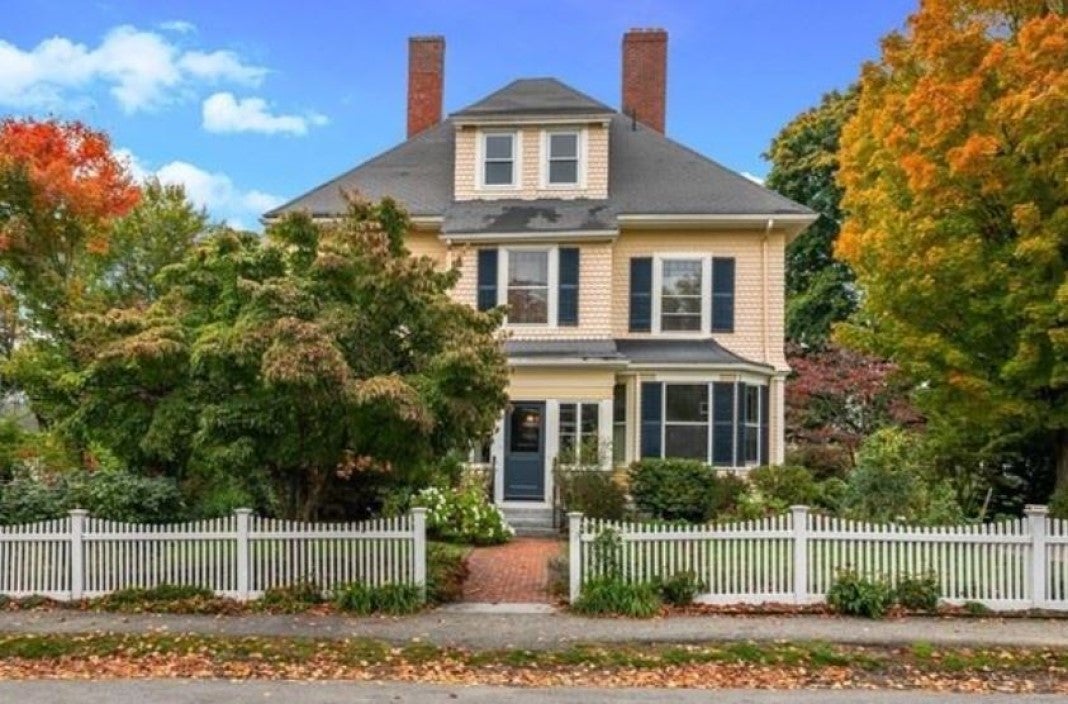 A peach-colored Victorian with green shutters and a white picket fence.