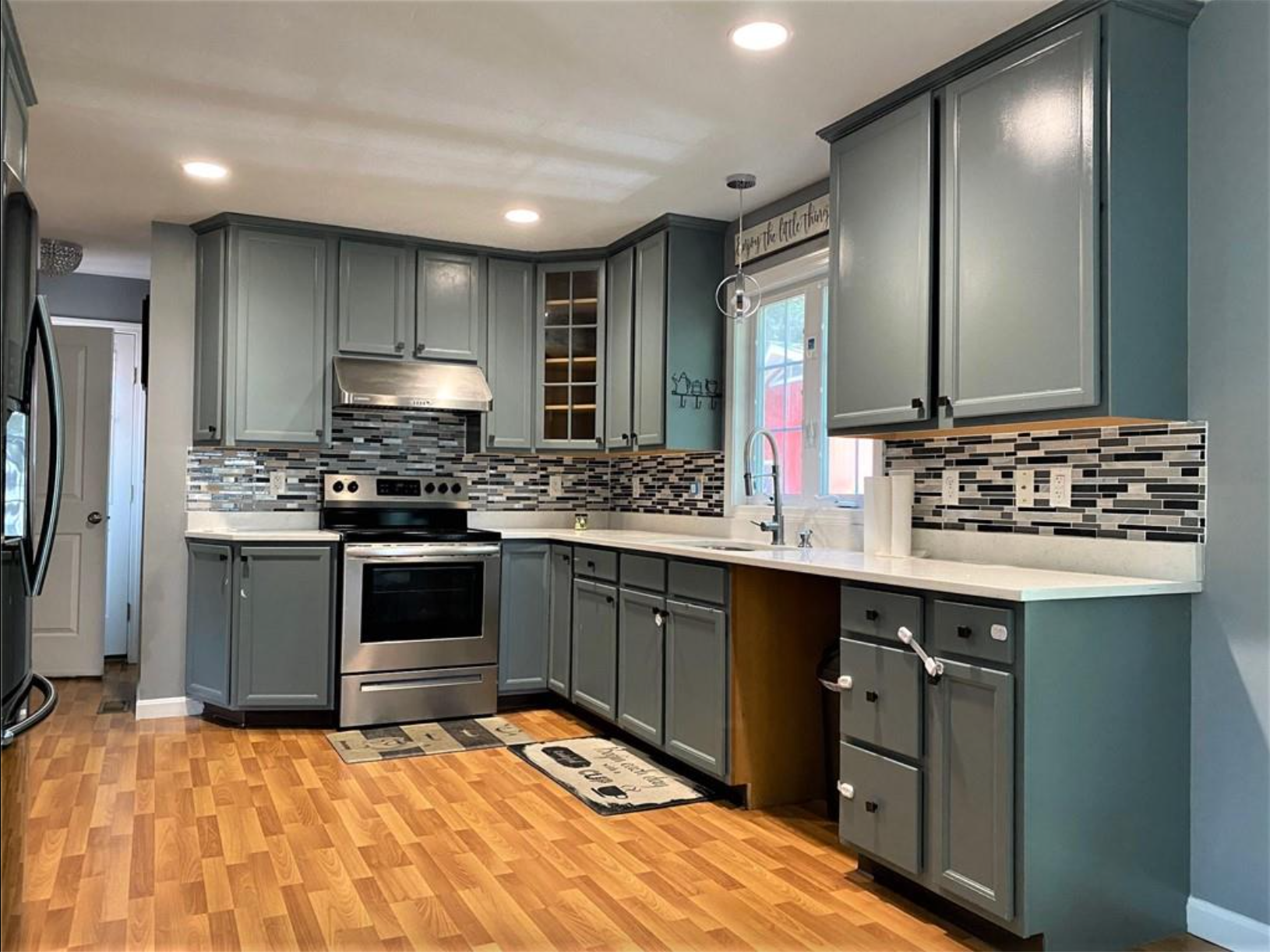 The kitchen has hardwood floors and stainless steel appliances with teal cabinets and a window above the sink.