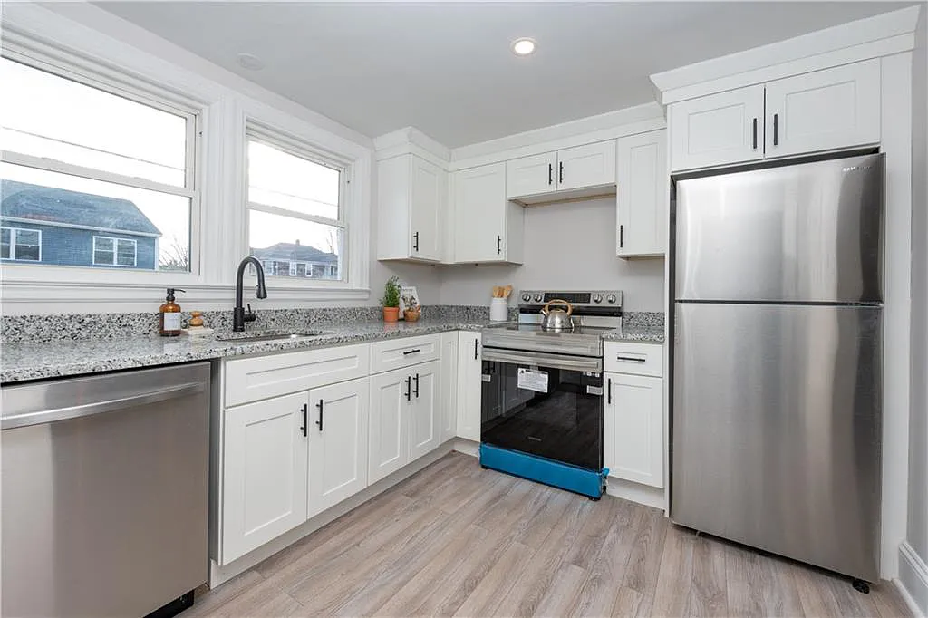 The kitchen has white Shaker-style cabinets, stainless steel appliances and double-hung windows above the sink.