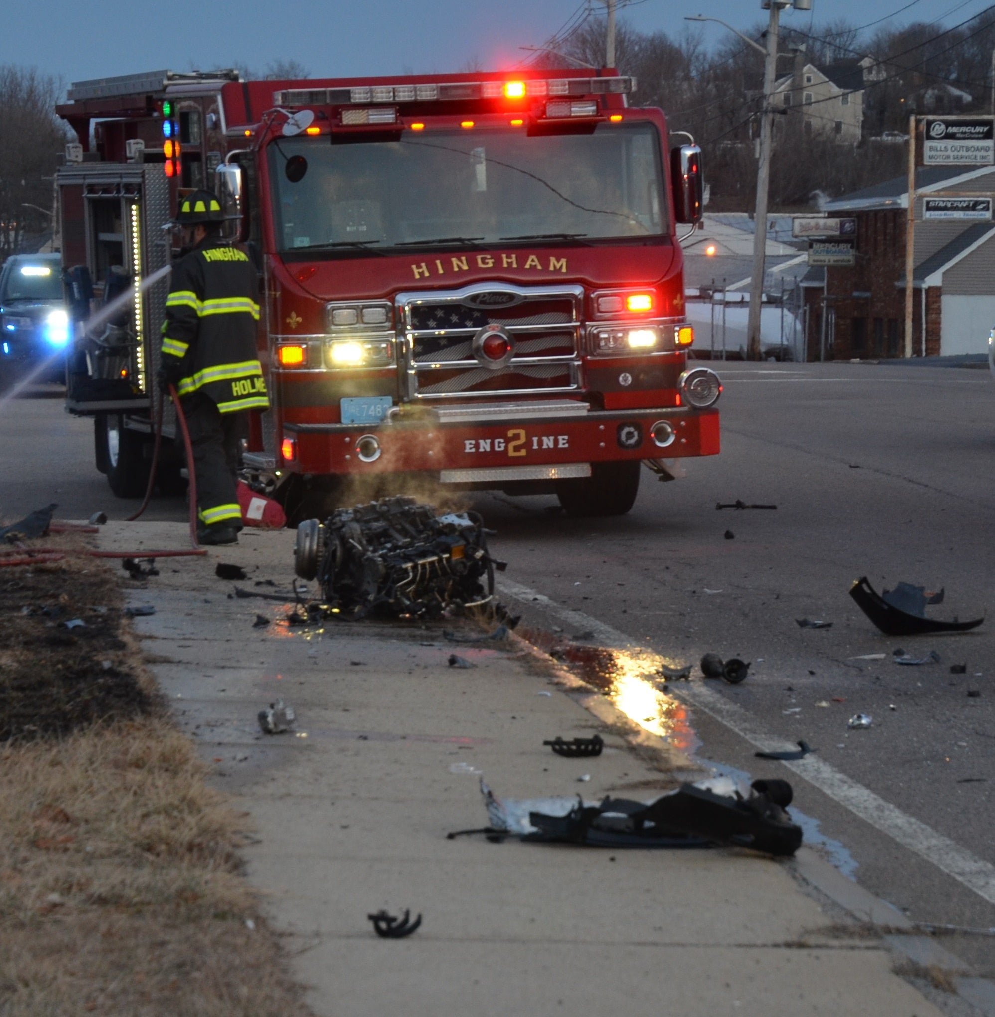 alt = A Hingham firetruck and firefighter at the scene of a crash on on Lincoln Street (Route 3A) at the intersection of Shipyard Drive Sunday. Debris from the crash is seen on the road in front of the truck.