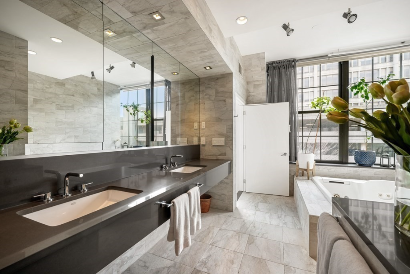 The bathroom has a double vanity and tile floors with floor-to-ceiling picture windows and views of the city.
