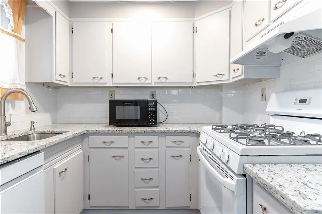 The kitchen is all white, with white cabinets and appliances, bright subway tile backsplash and granite countertops.