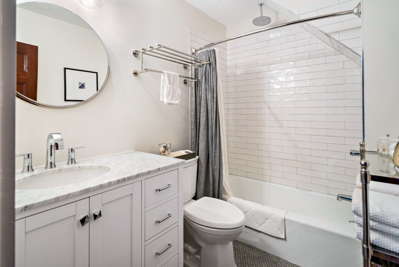The bathroom has a combination shower bathtub with white tiling and a single vanity.
