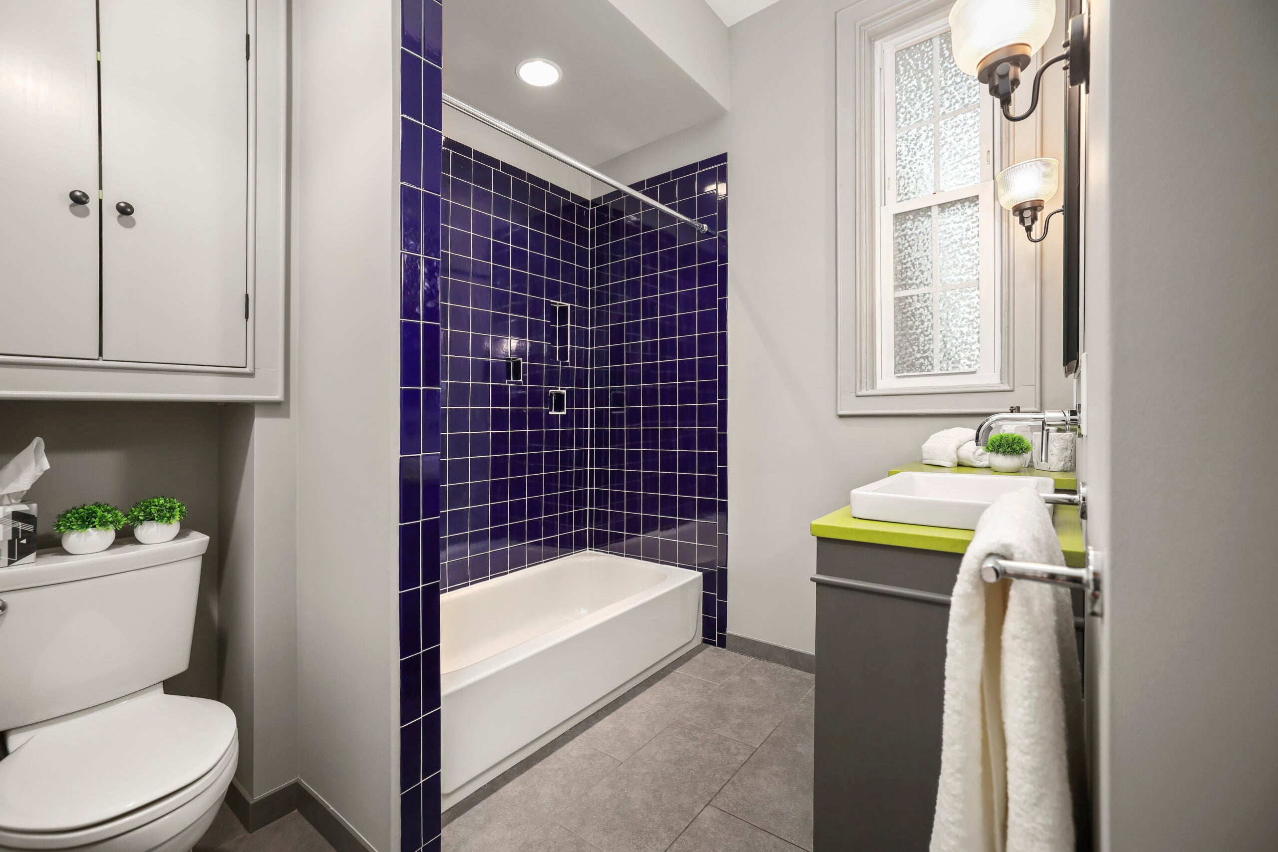 The bathroom has a combination shower-bathtub with navy blue tiling and a single-hung window.
