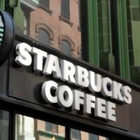 The green Starbucks logo is seen on a Boston storefront next to a white marquee sign reading "Starbucks Coffee."