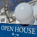 An open house sign with white lettering on a blue background. Balloons float overhead.
