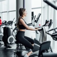 Adobe Stock photo of a woman in a gym riding a stationary bike in a sought-after condo amenity: a gym with a view.