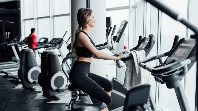 Adobe Stock photo of a woman in a gym riding a stationary bike in a sought-after condo amenity: a gym with a view.