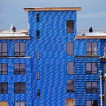 multi-story building under construction clad in blueboard