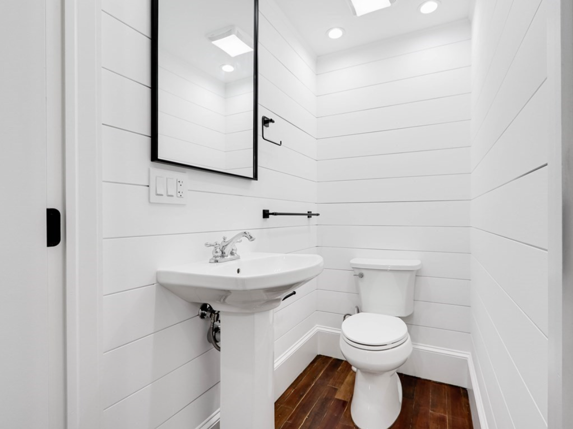 A bathroom with white walls and hardwood floors.