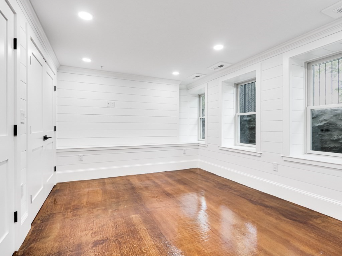 A primary bedroom with double-hung windows, two walk-in closets, hardwood floors and white walls.
