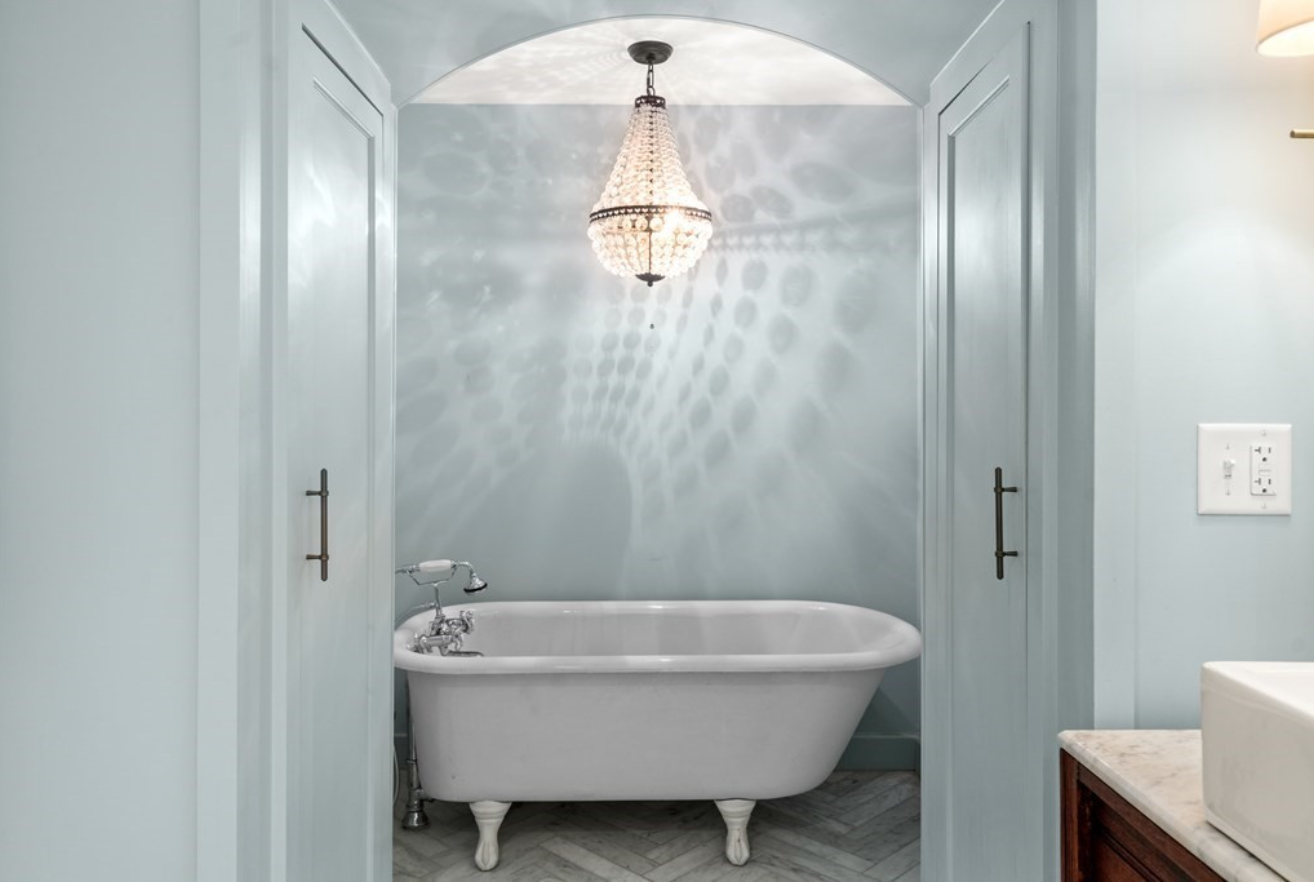 The standalone bathtub sits under a bejeweled chandelier.