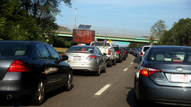 alt = cars sit in traffic on Route 3 in Massachusetts. A travel-time sign notes that I-93 is 5 miles or 14 minutes away.