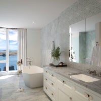 A view of a marble bath with white cabinets, a soaking tub, and a floor-to-ceiling window.