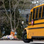 A school bus drives past a makeshift shrine with flowers and toys at the home of Lindsay Clancy, 32, who is accused of fatally strangling her daughter, Cora, 5, son Dawson, 3, and infant Callan last month.