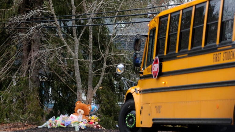 A school bus drives past a makeshift shrine with flowers and toys at the home of Lindsay Clancy, 32, who is accused of fatally strangling her daughter, Cora, 5, son Dawson, 3, and infant Callan last month.