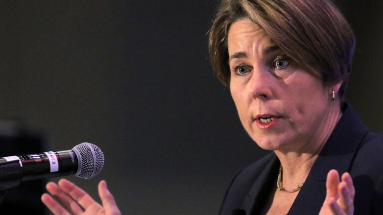alt = Maura Healey speaks while standing at a microphone