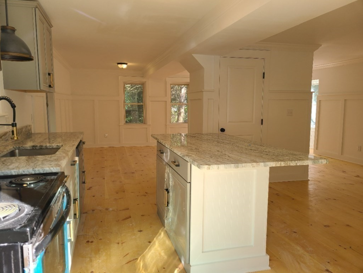 The kitchen has white walls, hardwood floors, stainless steel appliances and an island with seating.