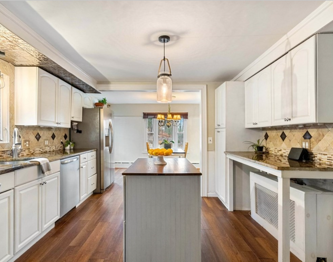 The kitchen has white walls, hardwood floors, stainless steel appliances and pendant lighting above the island.