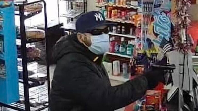 A man wearing a Yankees cap holds a gun during a robbery at a Hingham convenience store.